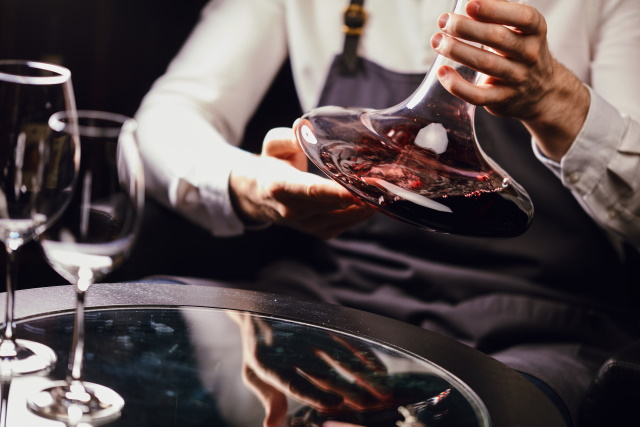 Sommelier holding a decanter of red wines next to a tray of empty wine glasses